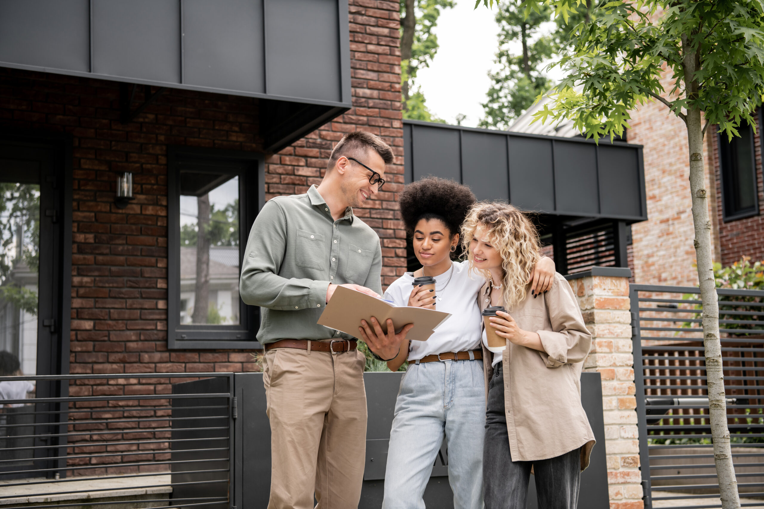 A property surveyor reviewing documents with a couple outside a modern house, discussing a RICS home survey level 2 report.